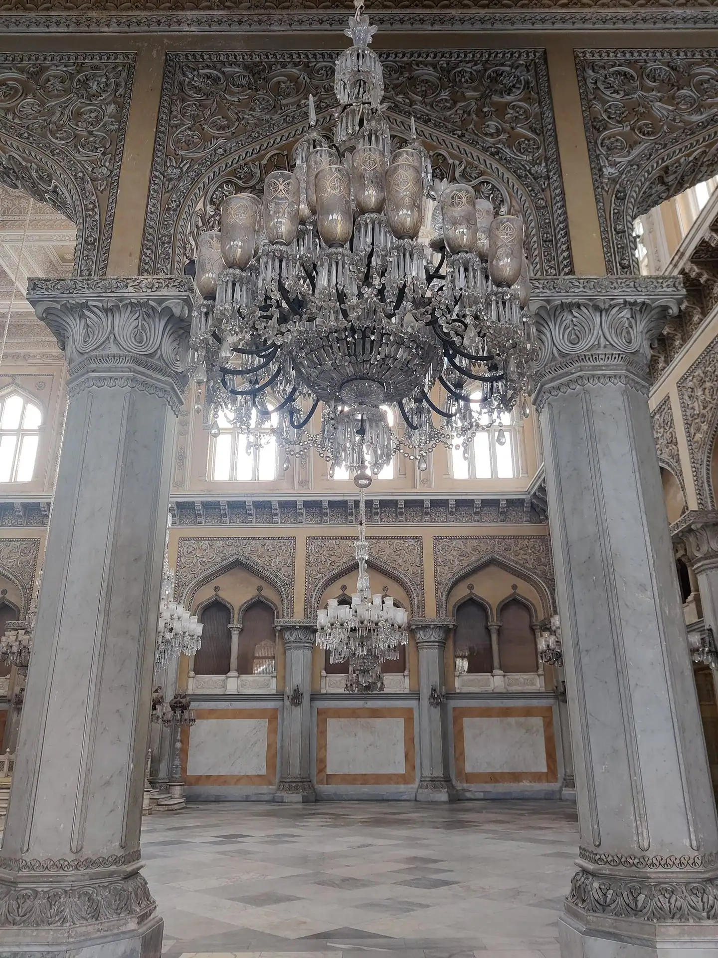 A crystal chandelier between carved columns in a Hyderabadi durbar hall